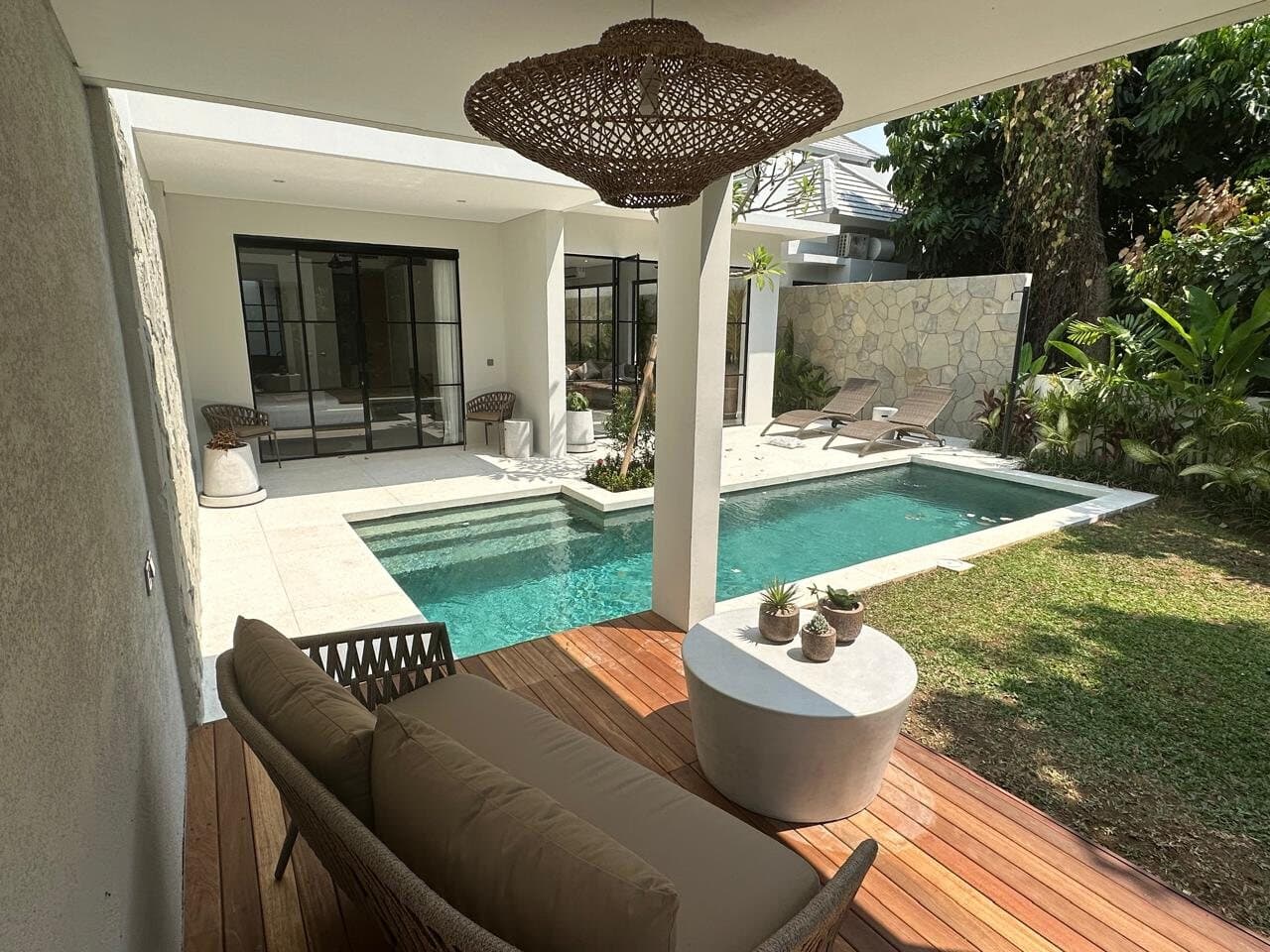 Covered terrace with a rattan pendant beside the pool and timber deck