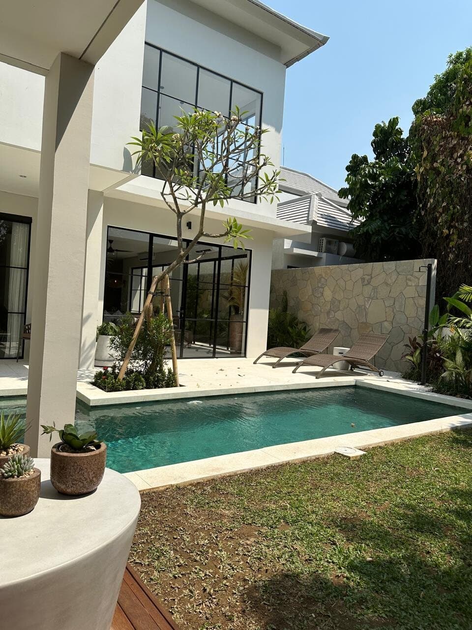 White two-storey villa with black steel windows and a pool, frangipani in front